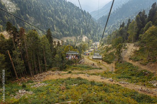 People climb up on a cable car high in the mountains. Green coniferous forest in the mountains in summer.