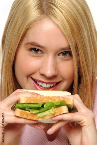 A blonde hair girl holding up a sandwich close to her face