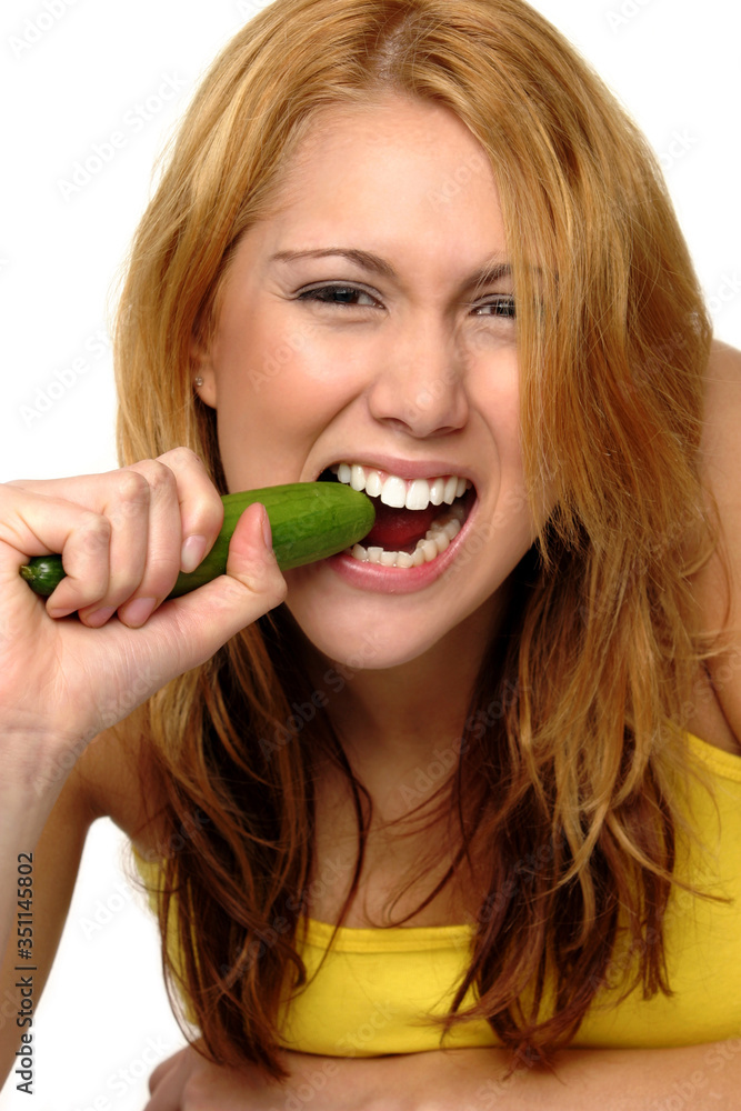 A woman in yellow spaghetti top biting a cucumber A woman in yellow spaghetti top biting a cucumber