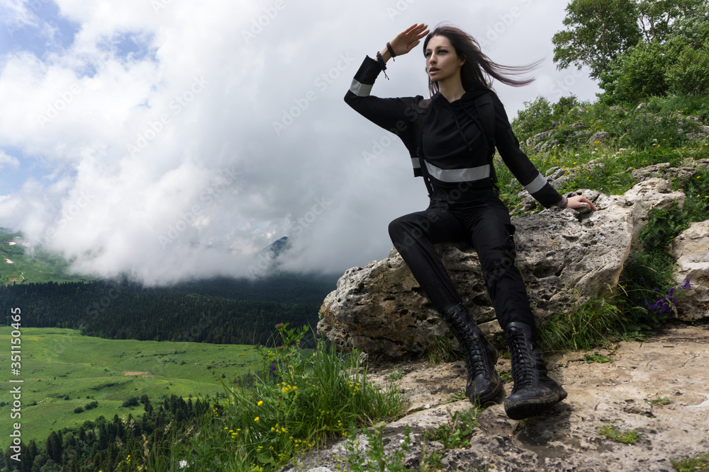 Young woman hiker sitting on the rock at the top of the mountain and looking forward with hand on forehead Young woman hiker sitting on the rock at the top of the mountain and looking forward with hand on forehead