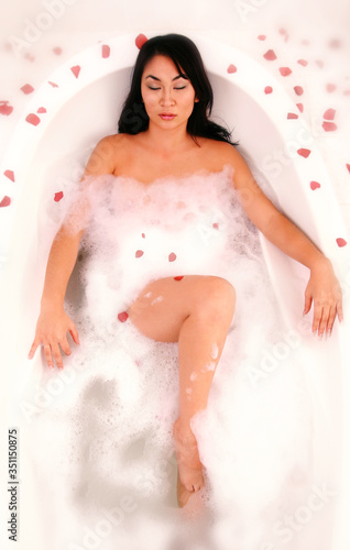 An Asian woman relaxing in a bathtub with rose petals everywhere