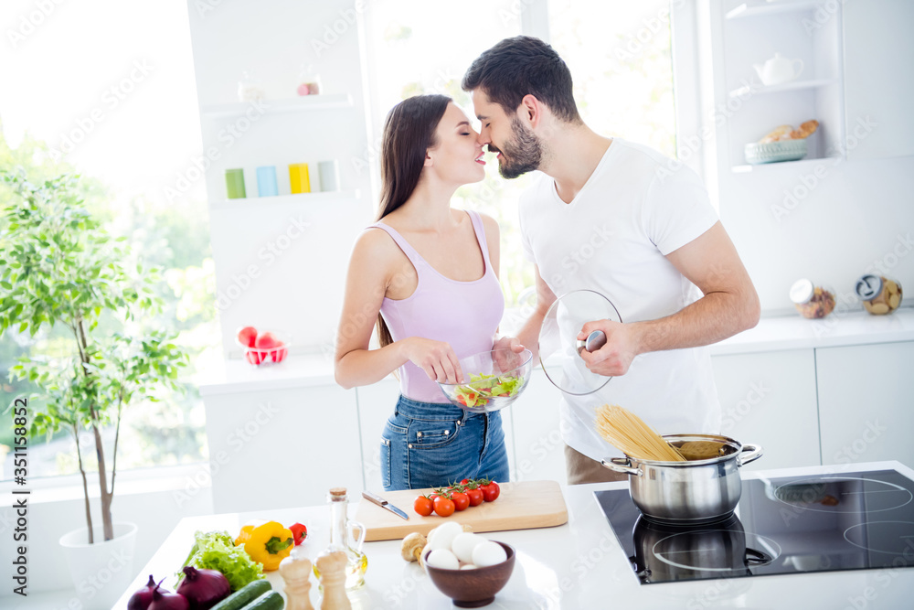 Photo of two people passionate tender gentle spouses prepare valentine day date dish nutrition woman hold bowl salad man boil macaroni kiss romance in kitchen house indoors