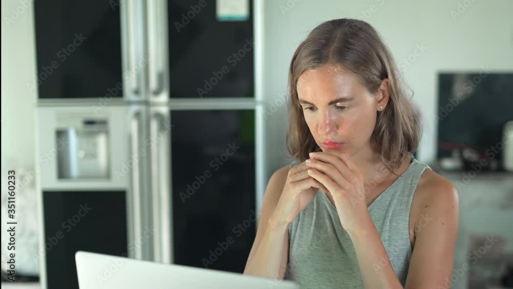 Girl with serious face watching on laptop computer screen sitting by table in kitchen Girl with serious face watching on laptop computer screen sitting by table in kitchen