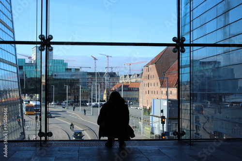 Silhouette of a young girl looking outside a big window on Copenaghen streets. Denmark buildings.
