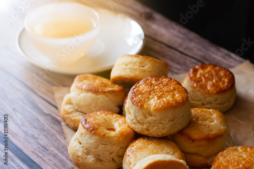 Close up homemade delicious dessert baked bread brown Traditional British Scones with blurred white cup of tea on wooden table and sunlight background.