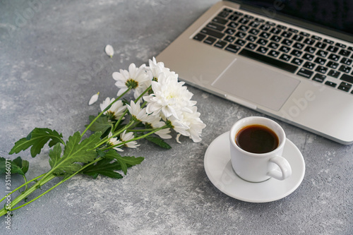 coffee mug, laptop and white chrysanthemums on the table on a gray background