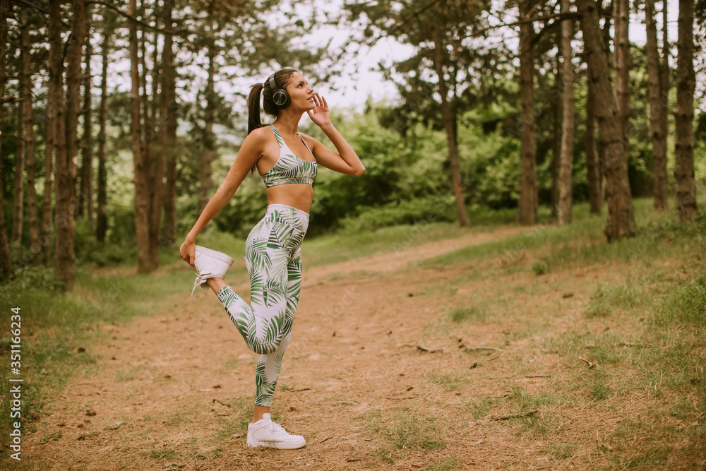 Young woman stretching and breathing fresh air in middle of forest while exercising