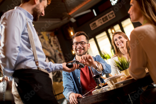 Young man paying with contactless credit card in restaurant after dinner