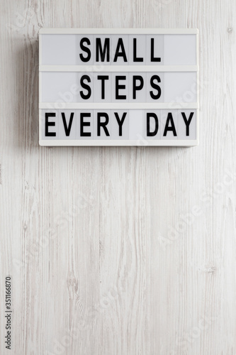 'Small steps every day' words on a modern board on a white wooden surface, top view. Overhead, from above, flat lay. Copy space.