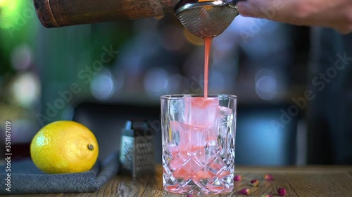 The red cocktail is pouring into the glass. Barman is pouring a red cocktail into the glass. The glass is on the table where the alcoholic cocktail is pouring. food styling restaurant