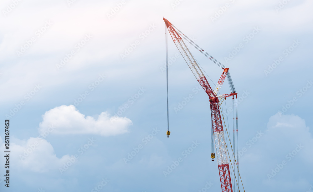 Construction crane against blue sky and white clouds. Real estate industry. Red-white crane use reel lift up equipment in construction site. Crane for rent. Crane dealership for construction business.