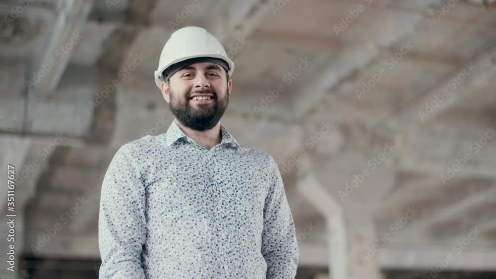 A young construction engineer in a helmet looks at the camera and smiles. Great design for any purpose. Safety. Indoors. Construction site. The concept of the construction industry. A young construction engineer in a helmet looks at the camera and smiles. Great design for any purpose. Safety. Indoors. Construction site. The concept of the construction industry.