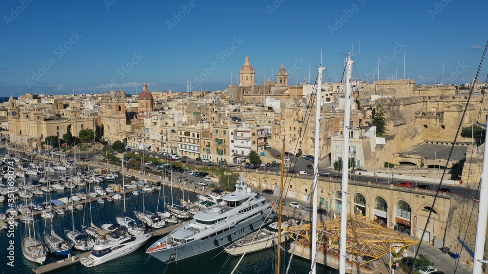 Aerial view of sailboats moored in harbour Senglea and Birgu, Bormla / Cospicua, Valletta, Malta. Ancient architecture of old town: christian orthodox churches, cathedrals, basilicas. Sunny day, blue 