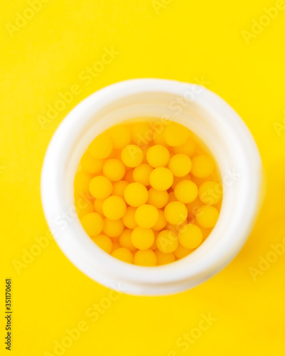 Pills of vitamin C in the opened white plastic container on bright yellow background. photo