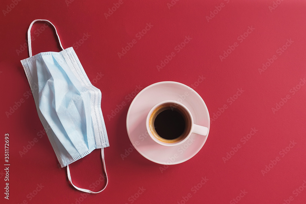 top view of a coffee cup and removed medical surgical mask on a red table. Concept of protection. Minimal concept of health and allergies.  space for a text.  - obrazy, fototapety, plakaty 