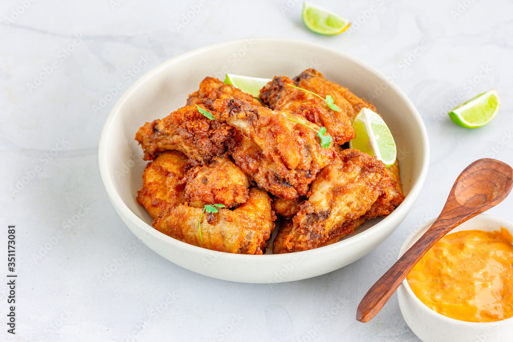 Oven Fried Crispy Chicken Wings in a White Bowl with Lemon and Dip Sauce on White Background Oven Fried Crispy Chicken Wings in a White Bowl with Lemon and Dip Sauce on White Background