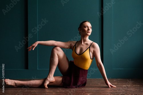Ballerina in dark bodysuit, in dress in dark interior Studio. Wall of bricks, piano.