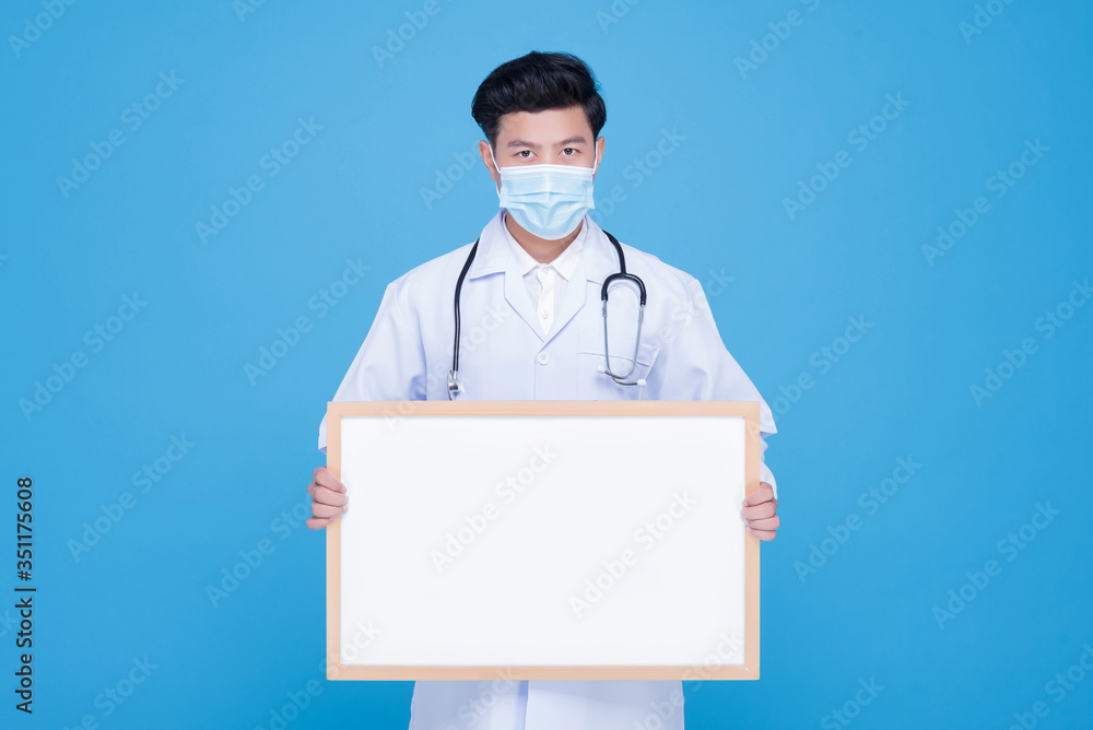 An Asian male doctor wears a surgical mask holding an empty whiteboard horizontally with both hands. An Asian male doctor wears a surgical mask holding an empty whiteboard horizontally with both hands.