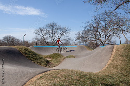 A teenager rides a bicycle on a pump track in a spring park, a guy goes in for sports