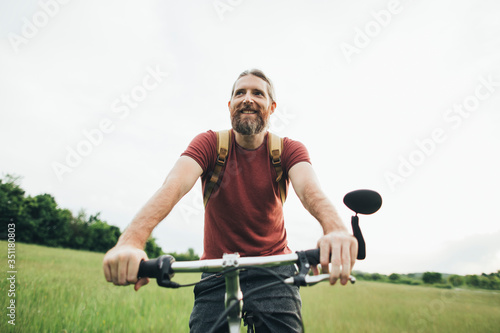 Bearded man with backpack riding bicycle in nature