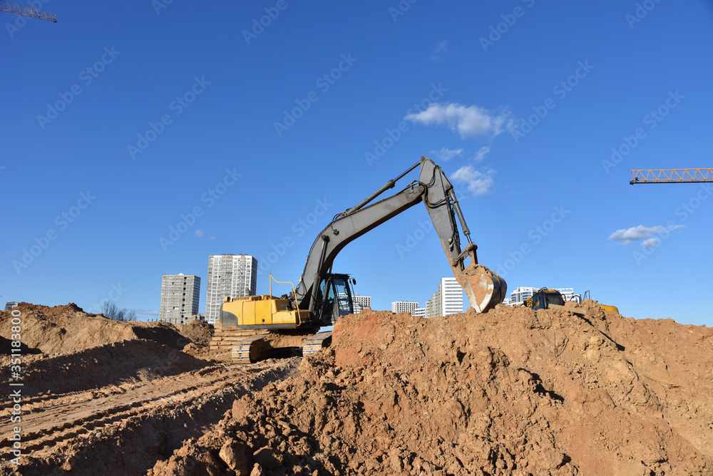 Excavator working at construction site on road work. Backhoe digs ground for the foundation and for paving out sewer line. Construction machinery for excavating, loading, lifting and hauling of cargo Excavator working at construction site on road work. Backhoe digs ground for the foundation and for paving out sewer line. Construction machinery for excavating, loading, lifting and hauling of cargo