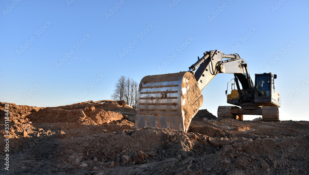 Yellow excavator during earthmoving at open pit on blue sky background. Construction machinery and earth-moving heavy equipment for excavation, loading, lifting and hauling of cargo on job sites