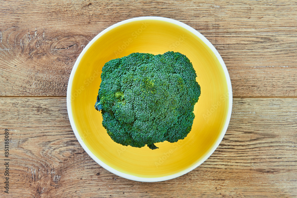 green broccoli inflorescence on a yellow plate on a wooden tabletop green broccoli inflorescence on a yellow plate on a wooden tabletop