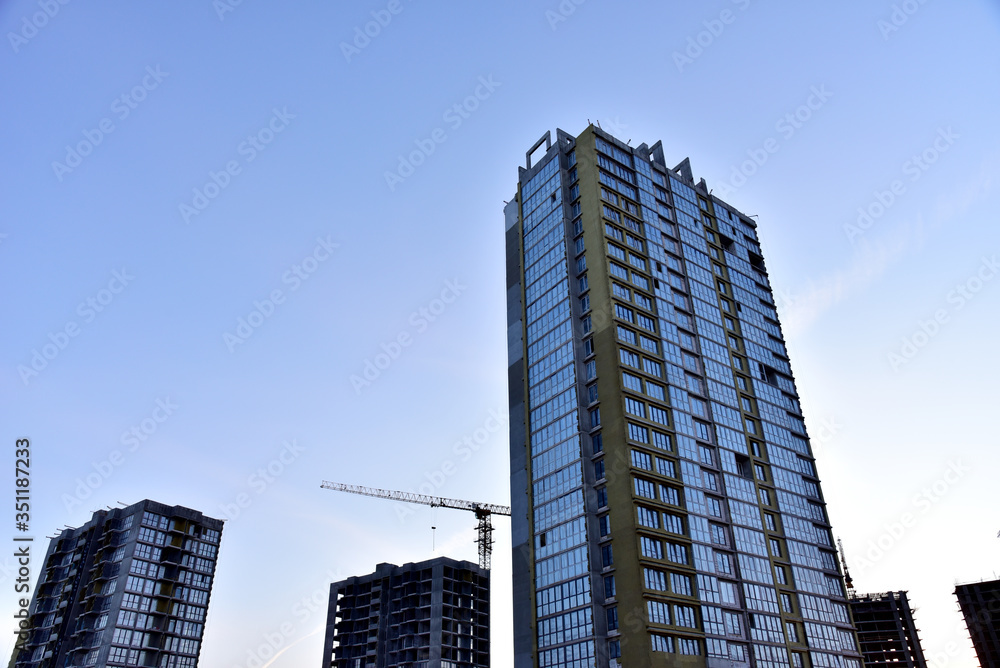 Tower cranes in action at construction site on sunset background. Thermal protection and Mineral wool insulation of the facade building. Installation double-glazed windows with frames Tower cranes in action at construction site on sunset background. Thermal protection and Mineral wool insulation of the facade building. Installation double-glazed windows with frames