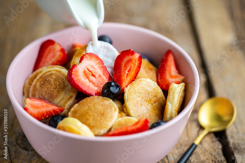  Pancake porridge, mini pancakes in a bowl with milk and maple syrup. Dutch mini-pancakes are called strawberry-potato pancakes. They are minced on mini-pancakes with strawberries and blueberries.