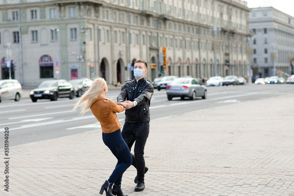 Obraz premium Couple in protective masks have a walk outdoors in the city near business building at quarantine time. Conception of coronavirus.