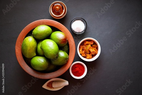 Homemade Raw green mango pickle. Preparation for spicy Kairiche lonche or aam ka achar. Ingredients at background such as, raw mango, salt, red chili powder, oil and fenugreek seeds. copy space. moody photo