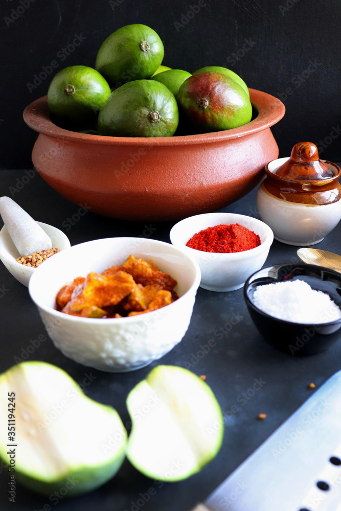 Homemade Raw green mango pickle. Preparation for spicy Kairiche lonche or aam ka achar. Ingredients at background such as, raw mango, salt, red chili powder, oil and fenugreek seeds. copy space. moody