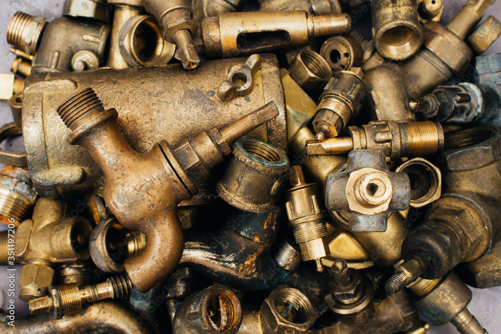 Brass scrap metal: taps, tees, plugs and various plumbing parts, spare parts. Against the background of a copper sheet. Close-up. Brass scrap metal: taps, tees, plugs and various plumbing parts, spare parts. Against the background of a copper sheet. Close-up.