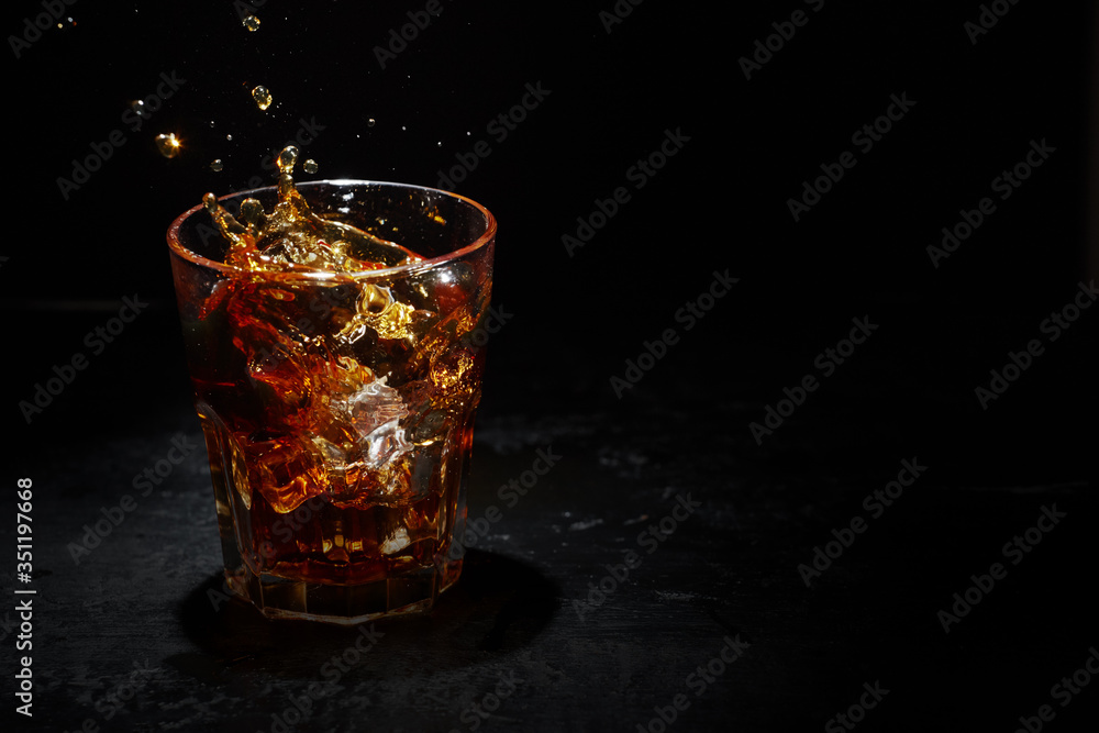 Splash of whiskey with ice in a glass with light behind. Place for text, copy-space.