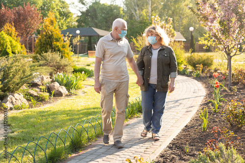 Happy elderly seniors couple wearing medical mask to protect from coronavirus in summer park