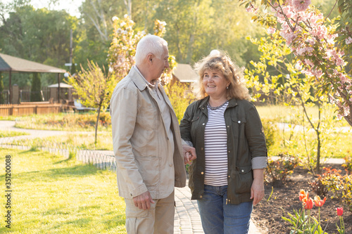 Senior elder caucasian couple together in park in spring or summer. Wife hugging husband smile with happiness. Beautiful love relation and care of retirement old people. © Marharyta
