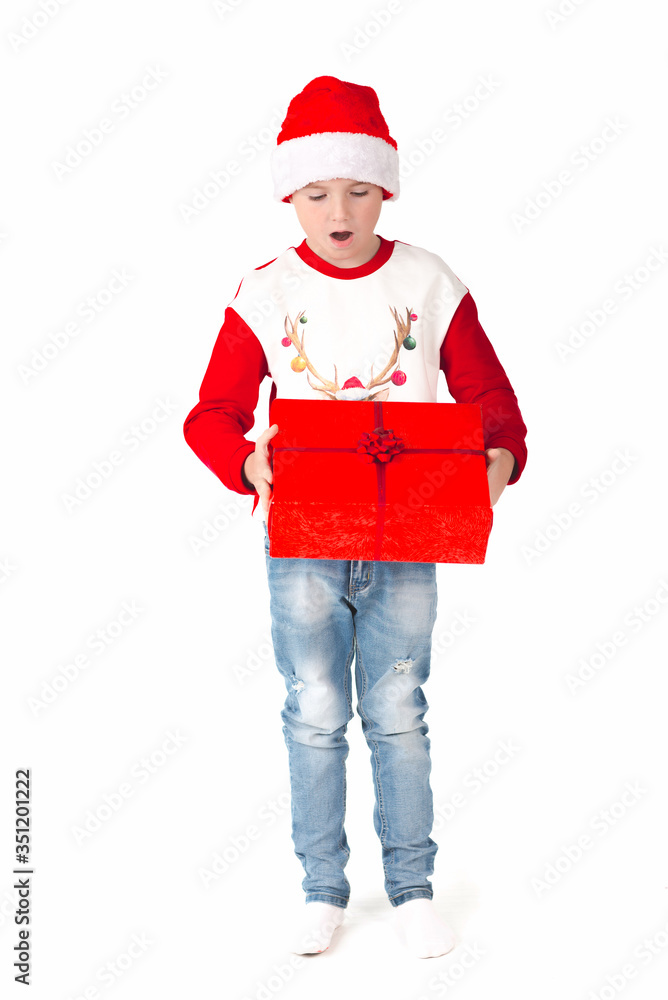 Merry christmas. Happy New Year. Caucasian young boy in Santa costume holds a red Christmas box.European teenaged boy in Santa Claus hat. White background. Merry christmas. Happy New Year. Caucasian young boy in Santa costume holds a red Christmas box.European teenaged boy in Santa Claus hat. White background.