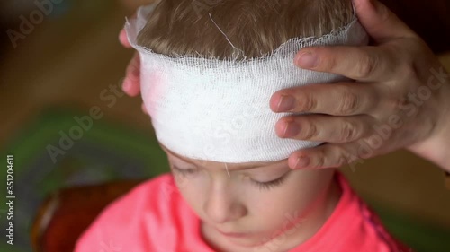 mother bandages the child's head. dressing an injured child's head. A pre-school boy with a head injury. Childhood trauma. Dissection of the scalp in preschool children
