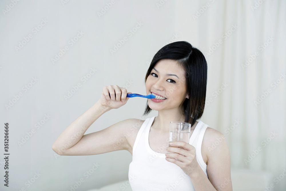 Woman brushing teeth while holding a glass of water Woman brushing teeth while holding a glass of water