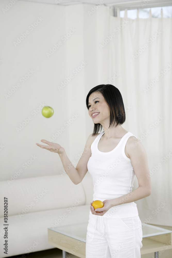 Woman throwing up apple while holding orange in another hand Woman throwing up apple while holding orange in another hand