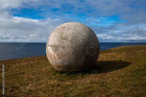 
landscape with the port of the island of grimsey in the north of iceland, off the arctic circle. The sky is loaded with clouds. A huge concrete ball is placed on a brown-green vegetation