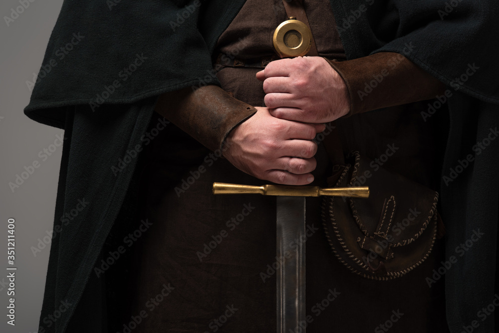 cropped view of medieval Scottish knight with sword in hands on grey background