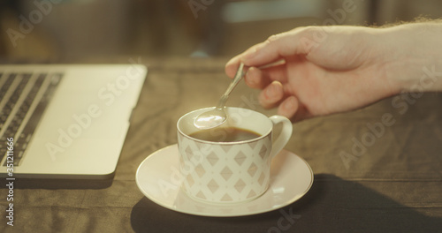 Man stirs his black coffee in the morning using a silver spoon (pulling the spoon up)