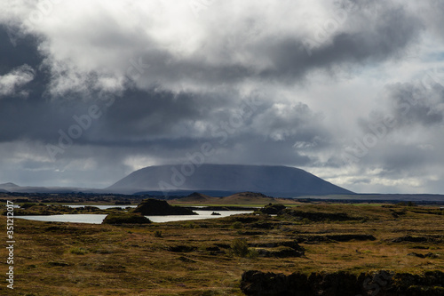 landscape in Iceland. The sky is loaded with clouds 
and there is a visible water point in the middle of volcanic stones full of moss photo