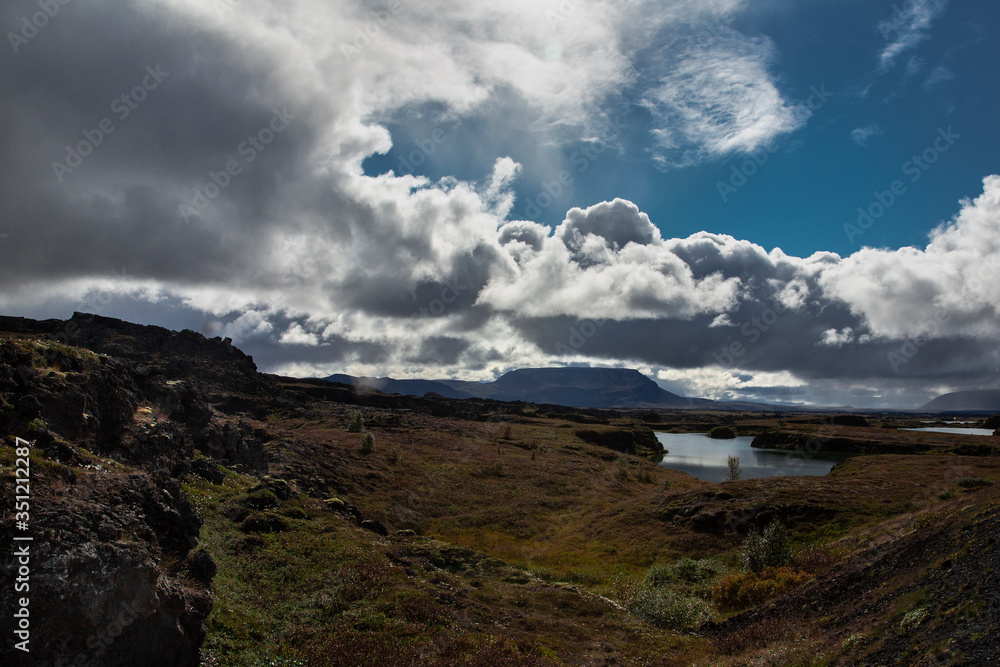 landscape in Iceland. The sky is loaded with clouds 
and there is a visible water point in the middle of volcanic stones full of moss