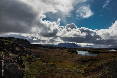 landscape in Iceland. The sky is loaded with clouds and there is a visible water point in the middle of volcanic stones full of moss