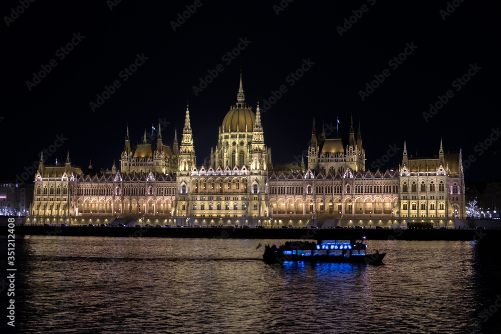 Obraz premium Beautiful illuminated famous Budapest parliament building along Danube River with cruise ships in the foreground, Budapest
