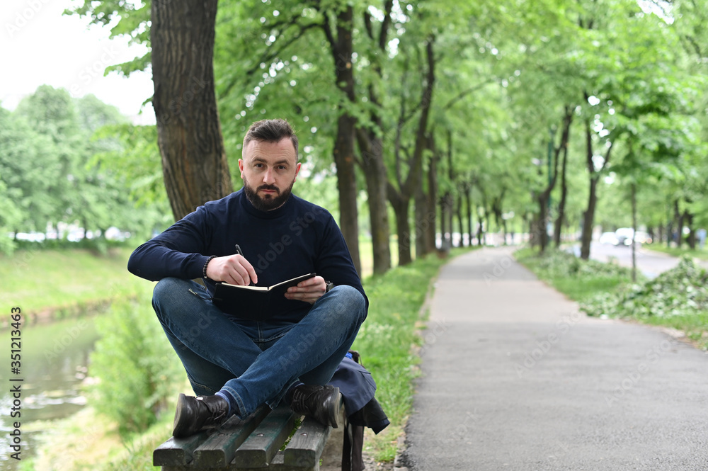 Obraz premium young man in park writing down ideas in notebook and enyoing in nature 