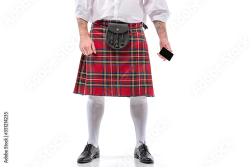 cropped view of Scottish man in red kilt with leather belt bag and smartphone on white background