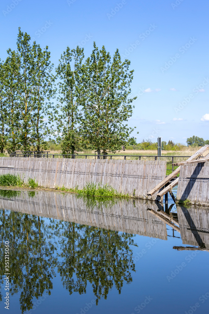 View of an historical weir system. In the background there is a row of poplars.